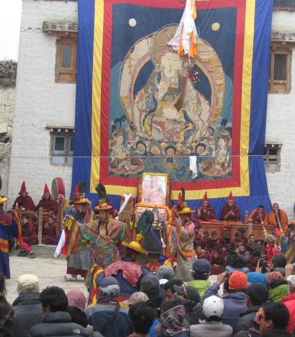 Masked monks performing traditional dances at the Tiji Festival in Lomanthang, Upper Mustang, Nepal, with Himalayan mountains in the background.