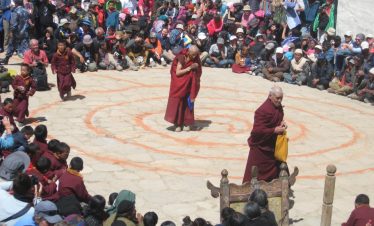 Masked monks performing traditional dances at the Tiji Festival in Lomanthang, Upper Mustang, Nepal, with Himalayan mountains in the background.