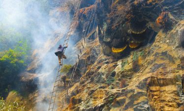 Adventurous honey collector climbs rocky cliff with smoke for wild bees in Nepal.