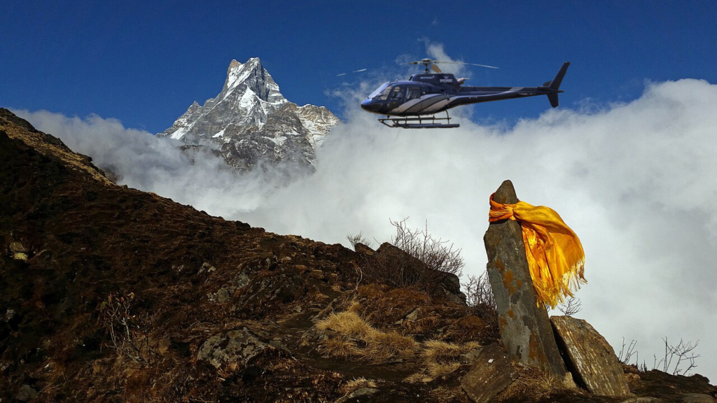 Helicopter flying over Mardi Himal Base Camp with snow-capped peaks, alpine meadows, and the Pokhara Valley below.