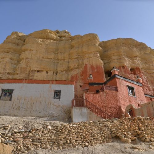 Ancient monastery built into rocky cliffs of Upper Mustang, Nepal under clear sky.