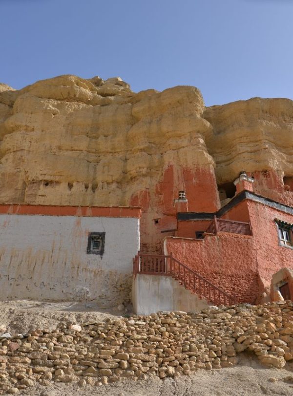 Ancient monastery built into rocky cliffs of Upper Mustang, Nepal under clear sky.