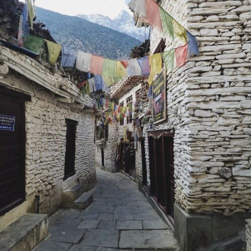 Picturesque stone alleyway with prayer flags in Mustang, Nepal, exuding peace and cultural charm.