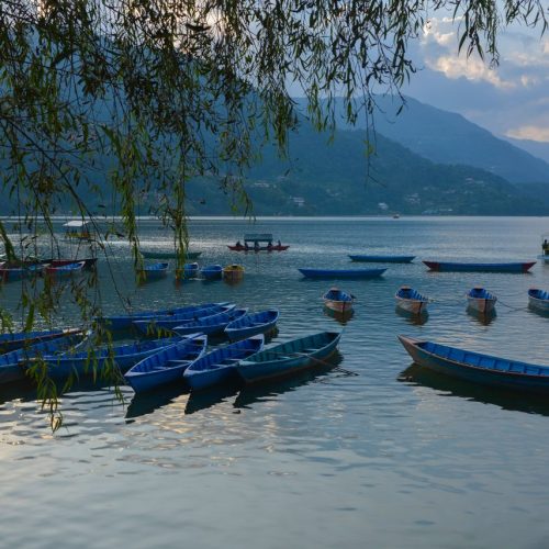 Peaceful scene of blue rowboats on a calm lake at sunset with mountain backdrop.